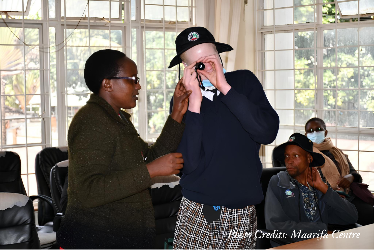 A girl with albinism holding a monocular close to her eye while a lady is standing next to her.